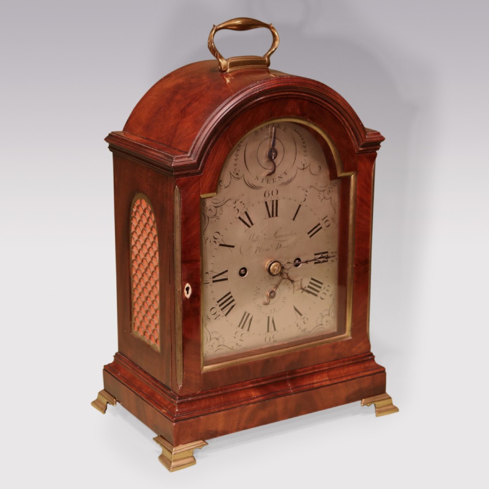 A George III mahogany bracket clock featuring an arched top with a brass carrying handle, an engraved silvered dial with Roman numerals, and brass bracket feet. View III