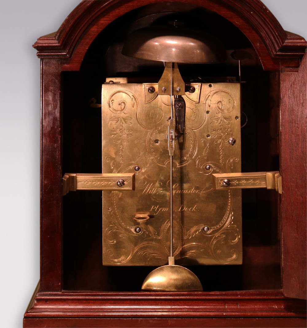 A George III mahogany bracket clock featuring an arched top with a brass carrying handle, an engraved silvered dial with Roman numerals, and brass bracket feet. View V