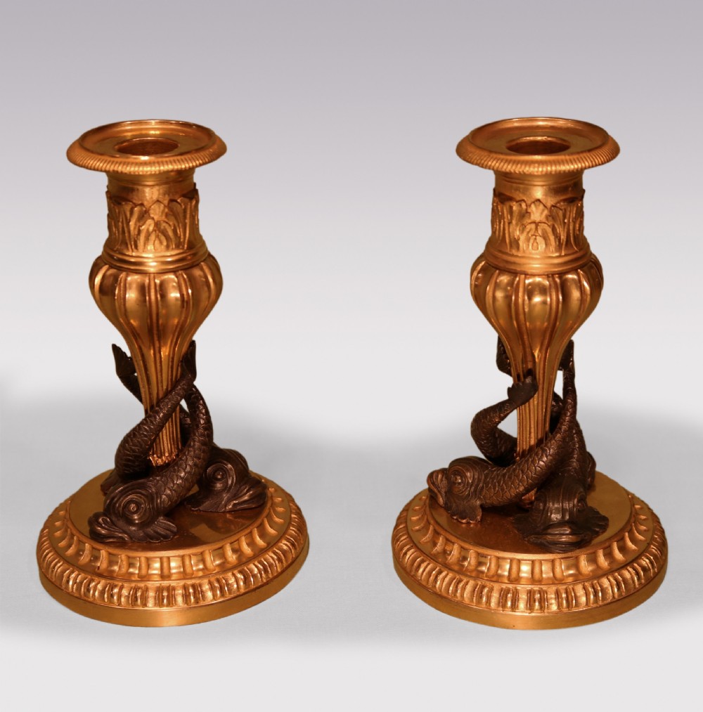 A pair of nineteenth-century gilt bronze and patinated bronze candlesticks featuring stylized dolphin figures wrapped around central fluted stems.