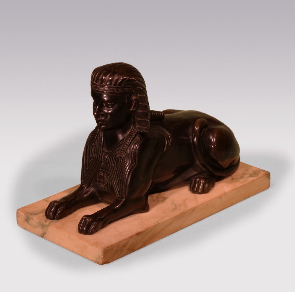 A Regency period dark bronze sphinx sculpture mounted on a rectangular veined cream marble base.