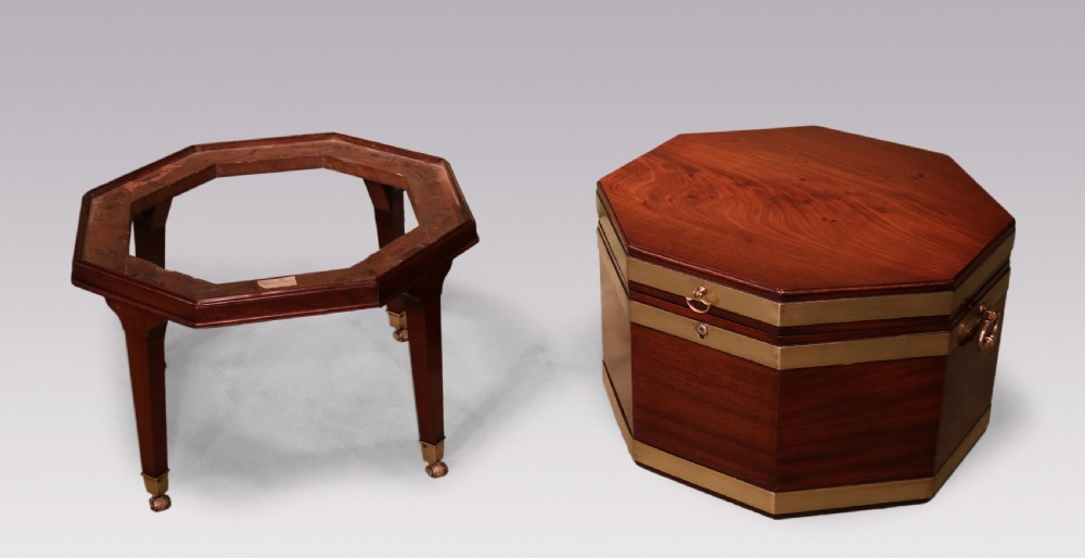 An octagonal George III mahogany wine cooler featuring brass straps, side drop handles, hinged lid, and tapered legs on castors. View V