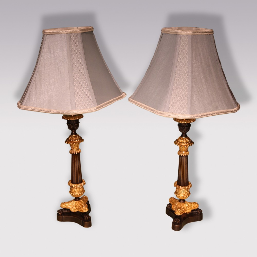 A symmetrical pair of antique patinated bronze and gilded ormolu candlestick table lamps with fluted shafts and light grey shades.