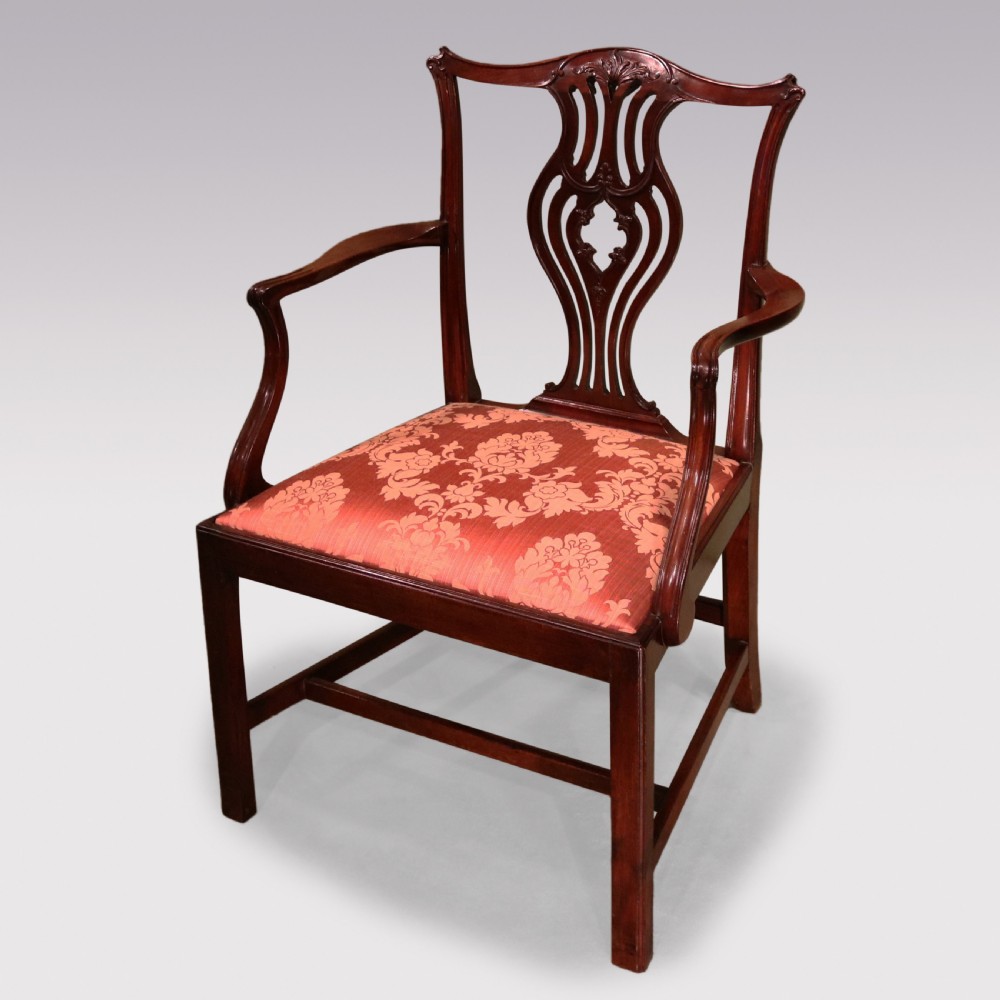 An 18th-century Chippendale carved mahogany armchair featuring a scrolled pierced splat, serpentine top rail, curved arms, and a patterned red damask seat.