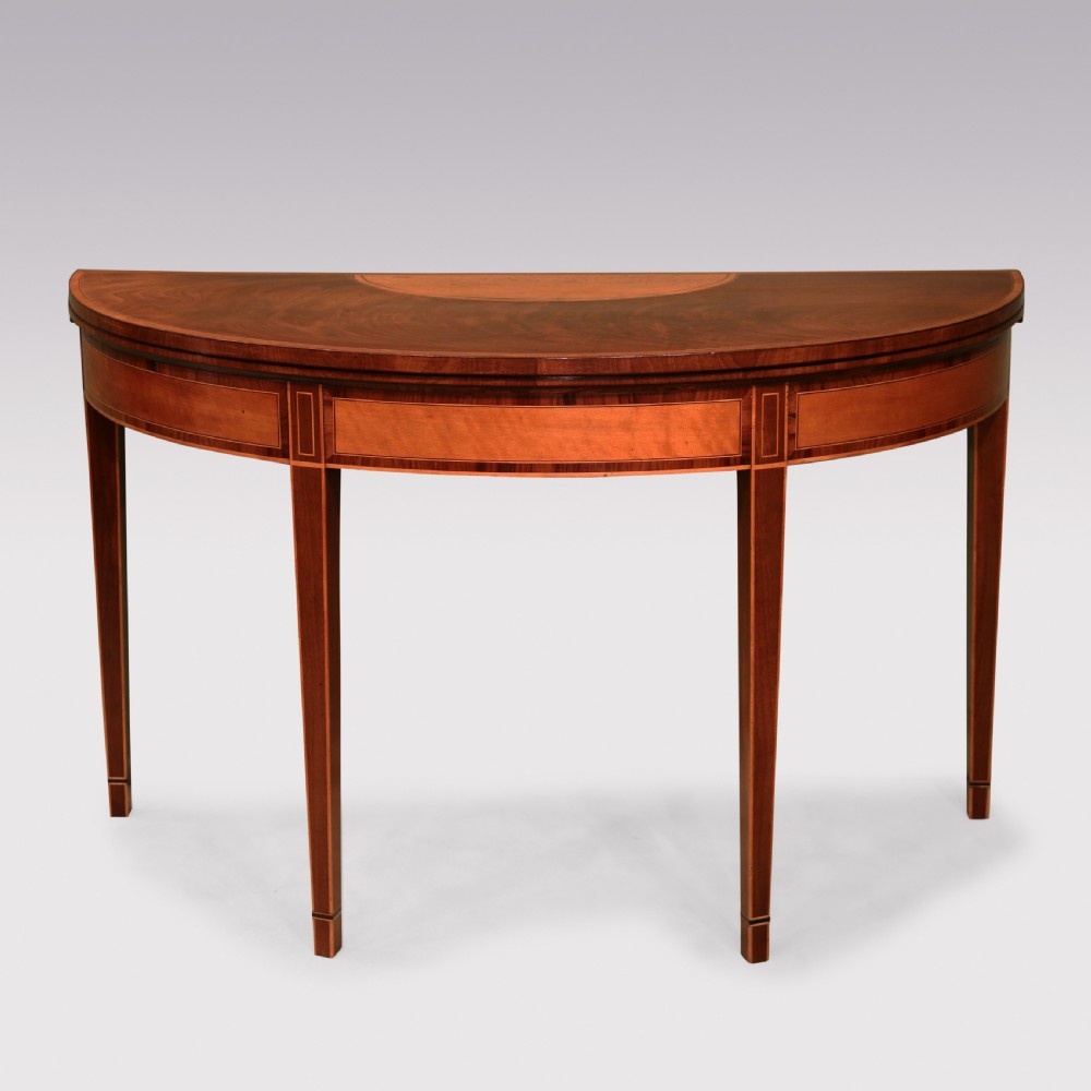 A demilune mahogany card table with satinwood crossbanding inlay and tapered square legs.
