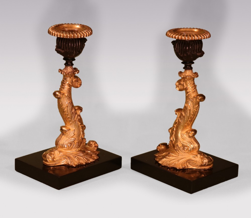 A pair of early nineteenth-century gilt bronze candlesticks featuring stylised dolphin stems resting on square black marble bases.