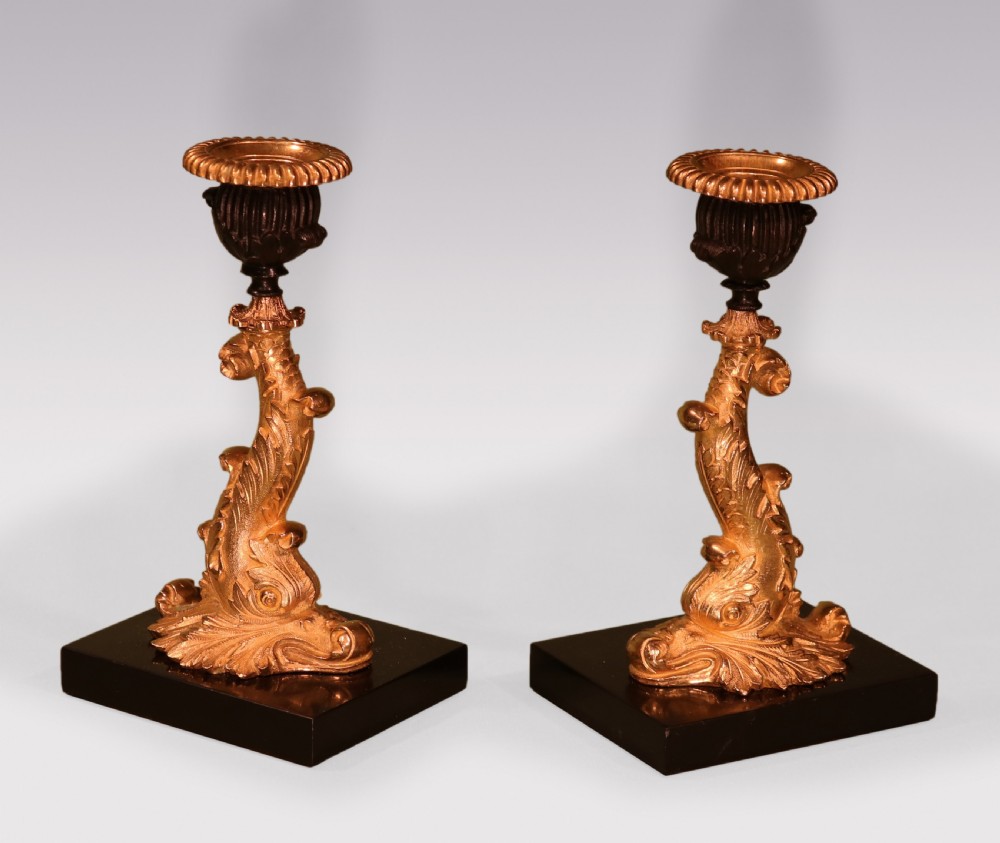 A pair of early nineteenth-century gilt bronze candlesticks featuring stylised dolphin stems resting on square black marble bases. View IV