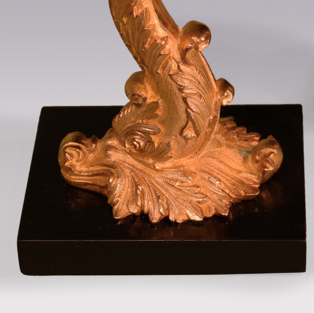 A pair of early nineteenth-century gilt bronze candlesticks featuring stylised dolphin stems resting on square black marble bases. View V