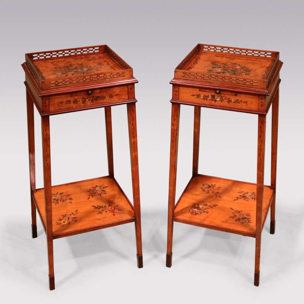 A pair of 19th-century satinwood kettle stands featuring open fretwork galleries, hand-painted floral decoration, pull-out slides, lower undertiers, and slender tapered legs.
