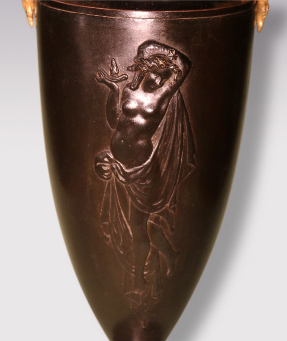 A pair of mid 19th-century dark patinated bronze urn-form table lamps featuring gilt handles, relief figures, circular bases, and cream pleated lampshades. View V