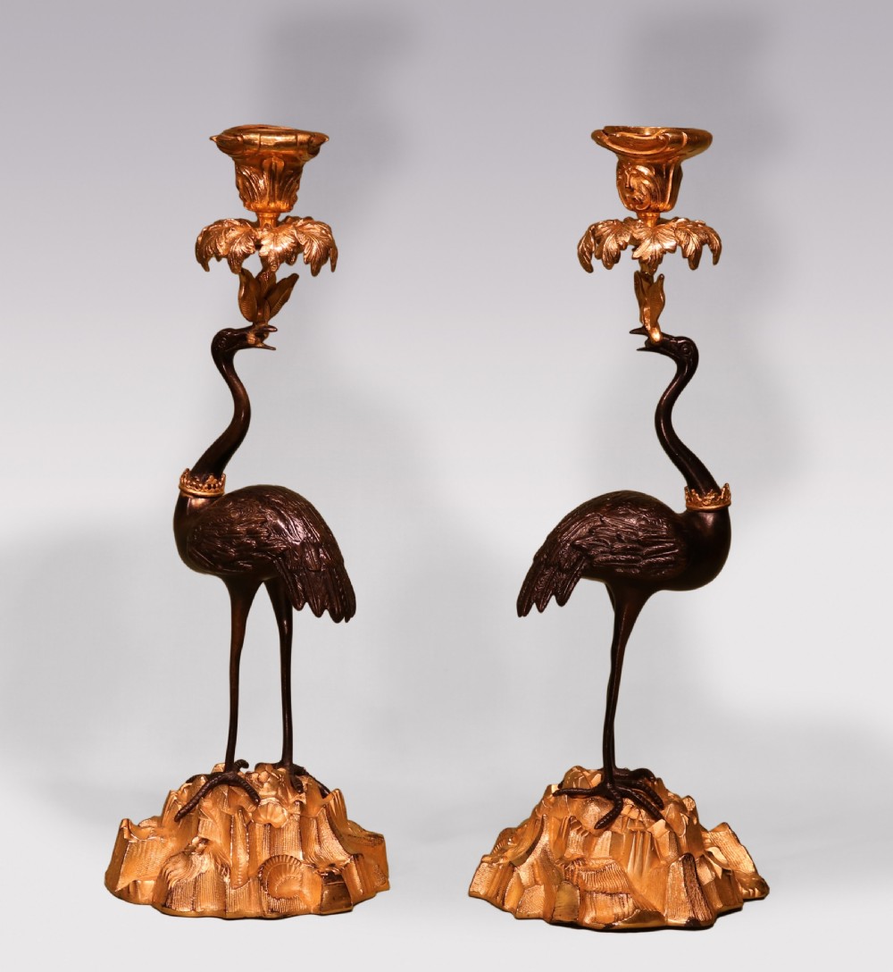 A pair of mid-19th century dark patinated bronze storks standing on rocky gilt ormolu bases, each holding a palm-leaf sconce in its beak.
