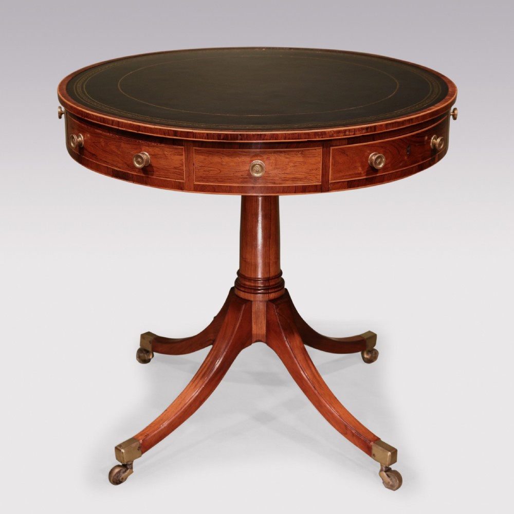 An antique Regency circular rosewood drum table featuring a dark leather inlaid top, perimeter drawers with brass knobs, and a central turned column on four splayed legs with brass castors.