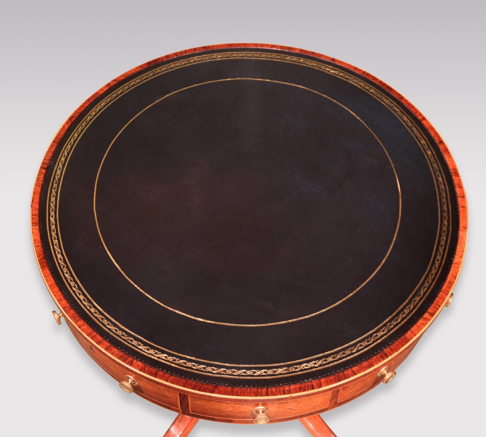 An antique Regency circular rosewood drum table featuring a dark leather inlaid top, perimeter drawers with brass knobs, and a central turned column on four splayed legs with brass castors. View II