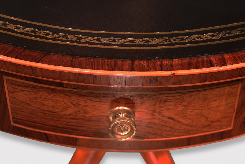 An antique Regency circular rosewood drum table featuring a dark leather inlaid top, perimeter drawers with brass knobs, and a central turned column on four splayed legs with brass castors. View III