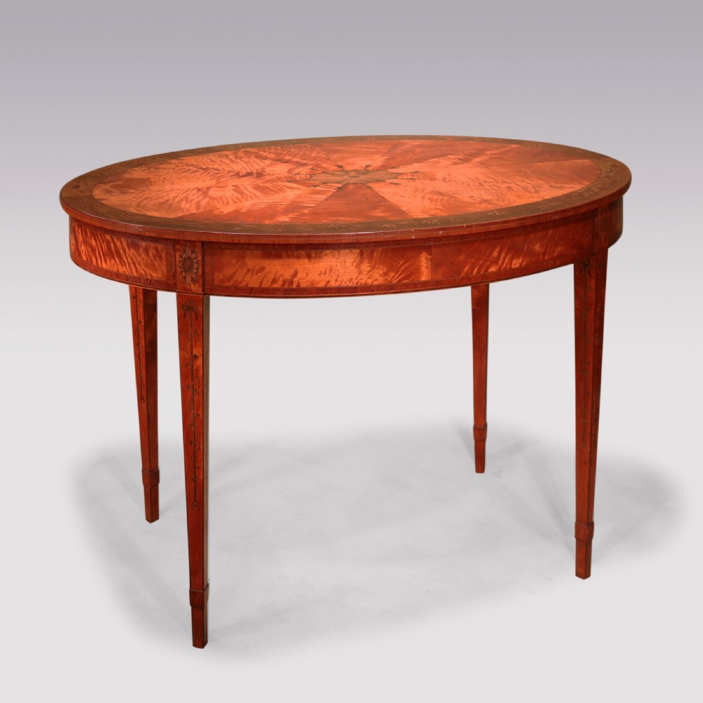 An oval antique satinwood occasional table featuring radial marquetry, crossbanded edges, an inlaid apron, and slender square tapered legs.