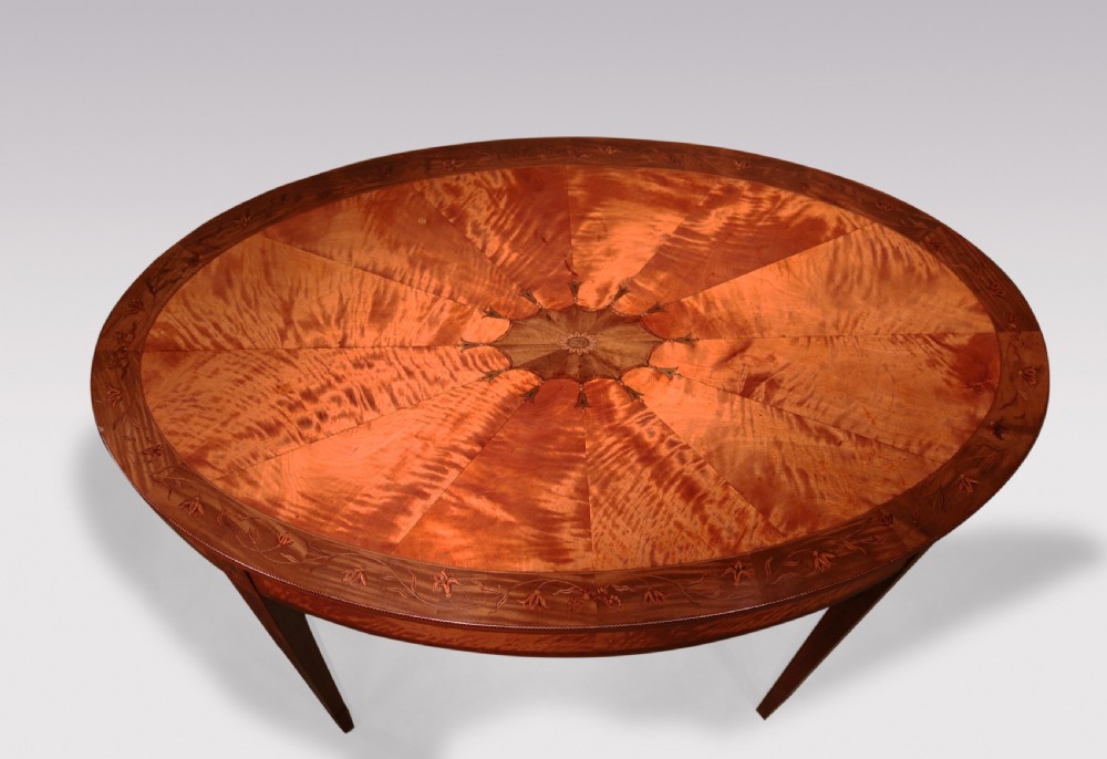An oval antique satinwood occasional table featuring radial marquetry, crossbanded edges, an inlaid apron, and slender square tapered legs. View IV