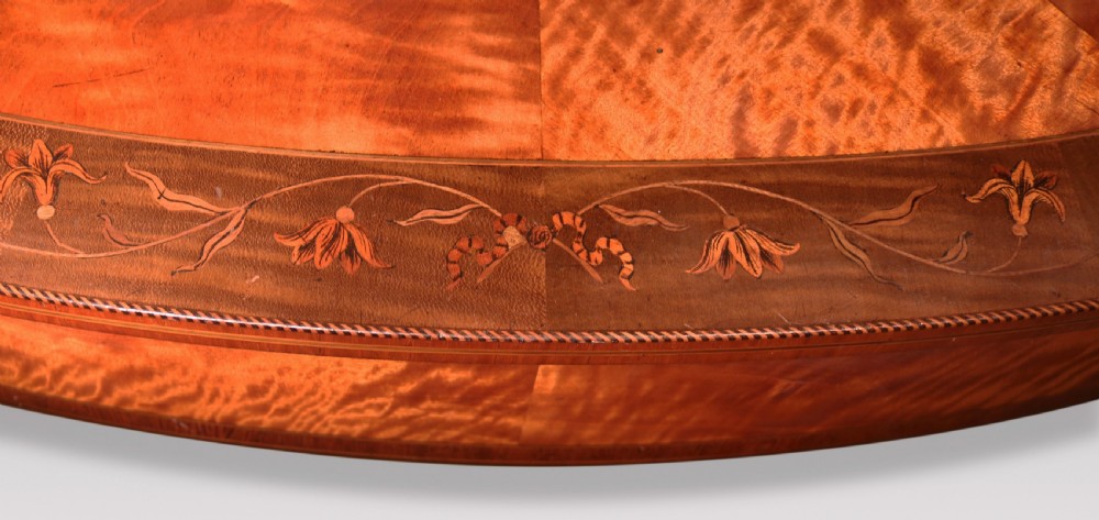 An oval antique satinwood occasional table featuring radial marquetry, crossbanded edges, an inlaid apron, and slender square tapered legs. View VI