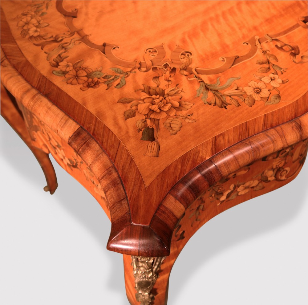 A mid-19th-century serpentine satinwood writing table featuring floral marquetry inlay, calamander banding, gilt-bronze mounts, and cabriole legs. View V