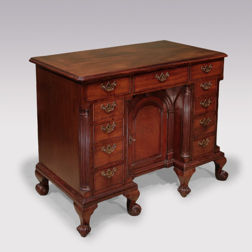 An antique George II mahogany kneehole desk featuring a recessed central cupboard, multiple brass-handled drawers, fluted quarter-columns, and carved scroll feet. View II