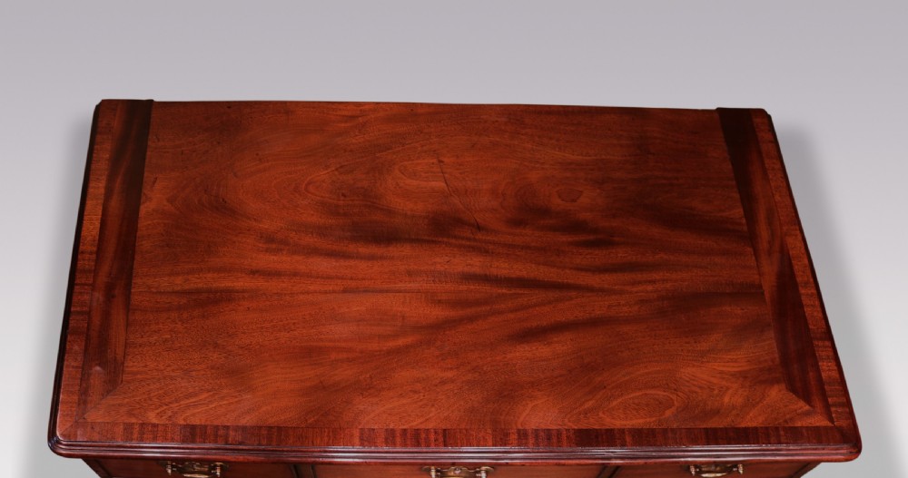 An antique George II mahogany kneehole desk featuring a recessed central cupboard, multiple brass-handled drawers, fluted quarter-columns, and carved scroll feet. View IV