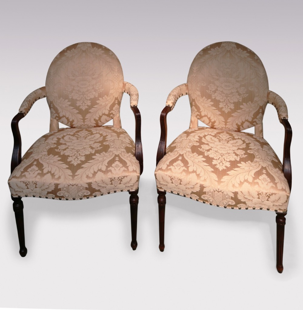 A pair of 18th-century mahogany armchairs upholstered in cream floral damask fabric with oval backrests and fluted legs.