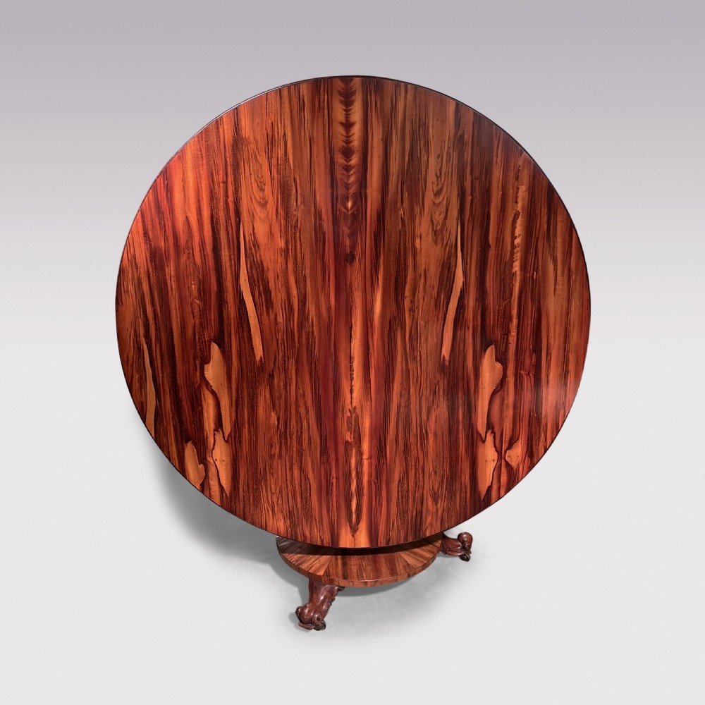 A circular William IV period tilt-top breakfast table featuring highly figured coromandel wood veneer mounted on a central pedestal base with carved feet.