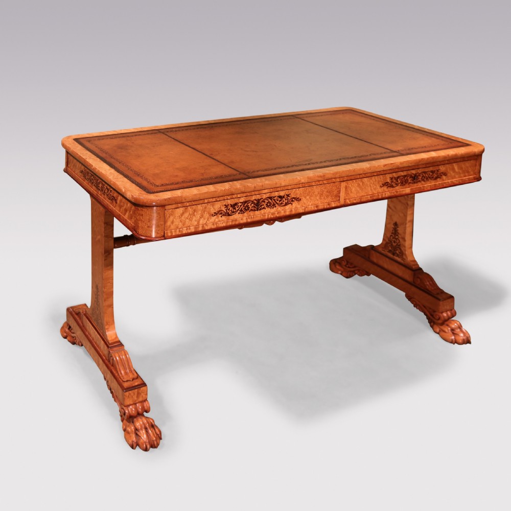 An early 19th-century birdseye maple writing table featuring a triple leather-tooled surface, inlaid floral aprons, and carved trestle legs.