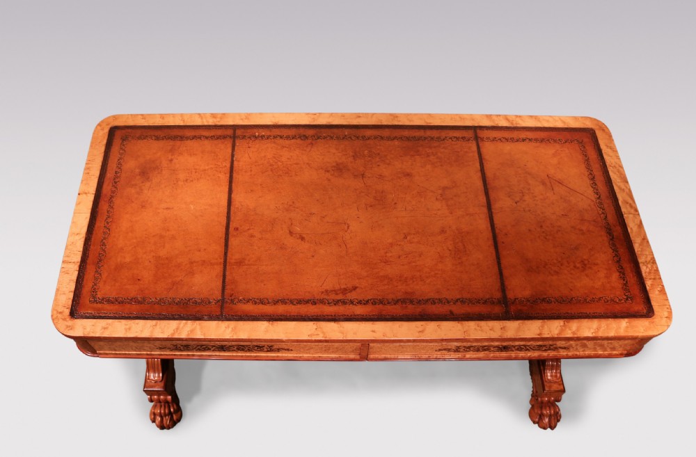 An early 19th-century birdseye maple writing table featuring a triple leather-tooled surface, inlaid floral aprons, and carved trestle legs. View III