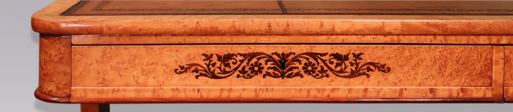 An early 19th-century birdseye maple writing table featuring a triple leather-tooled surface, inlaid floral aprons, and carved trestle legs. View VI