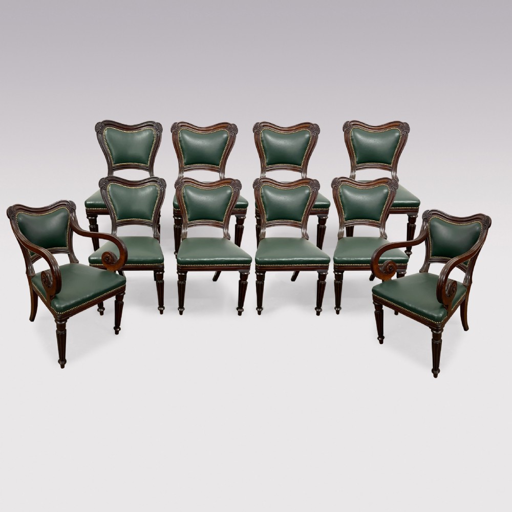A set of ten Victorian mahogany dining chairs upholstered in forest green leather with brass stud trimming, featuring turned reeded legs and scrollwork carved backs, including two carver armchairs.