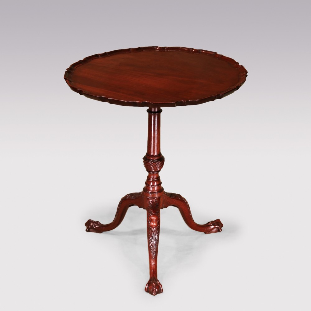A George III mahogany tripod table featuring a scalloped piecrust top, a turned pedestal stem, and three carved cabriole legs terminating in claw and ball feet.