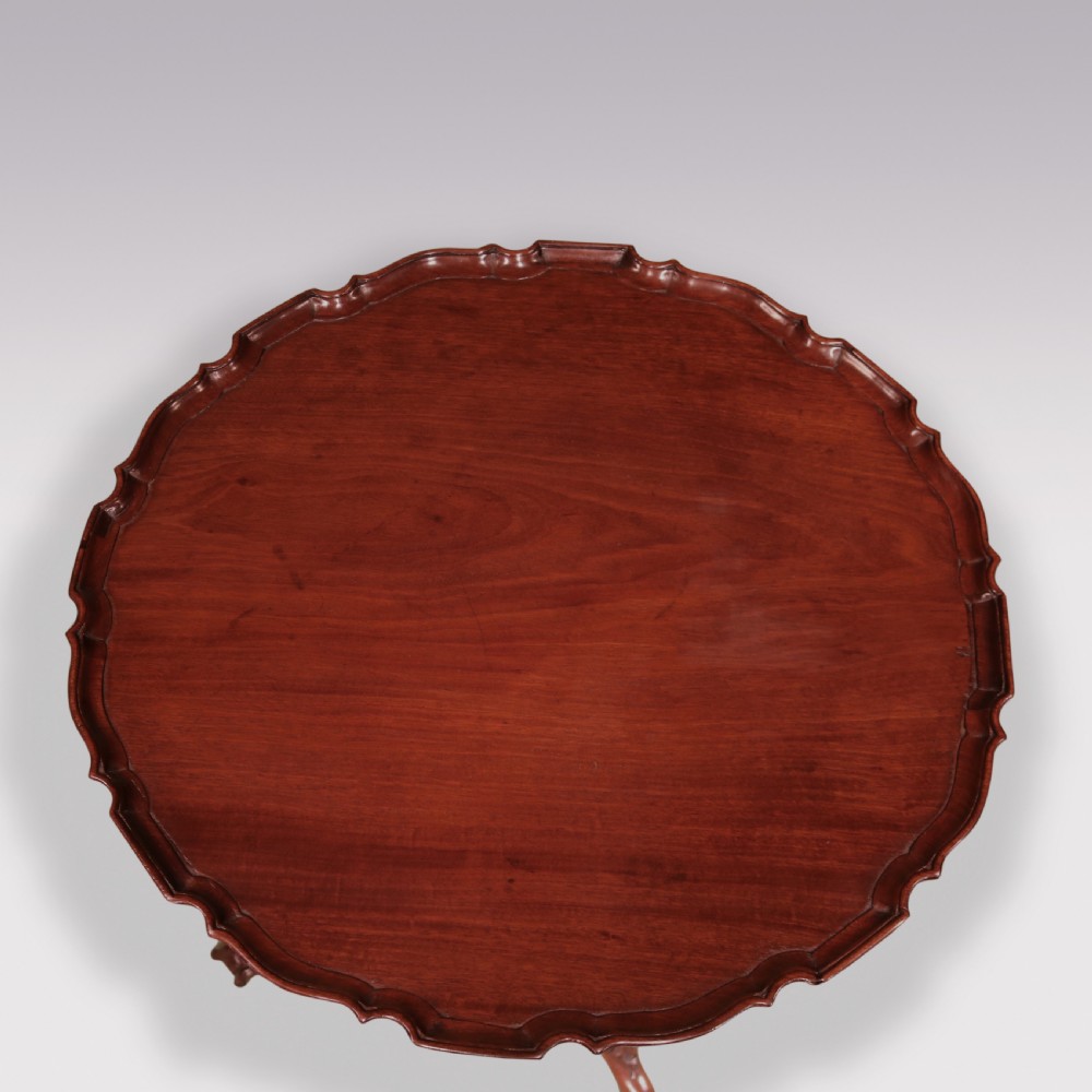 A George III mahogany tripod table featuring a scalloped piecrust top, a turned pedestal stem, and three carved cabriole legs terminating in claw and ball feet. View II