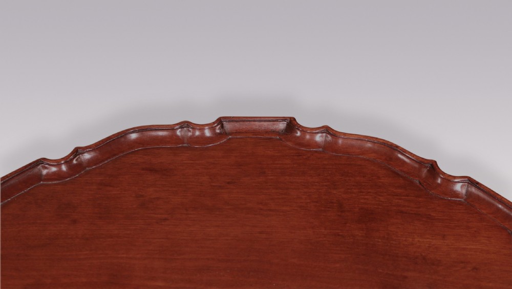 A George III mahogany tripod table featuring a scalloped piecrust top, a turned pedestal stem, and three carved cabriole legs terminating in claw and ball feet. View III