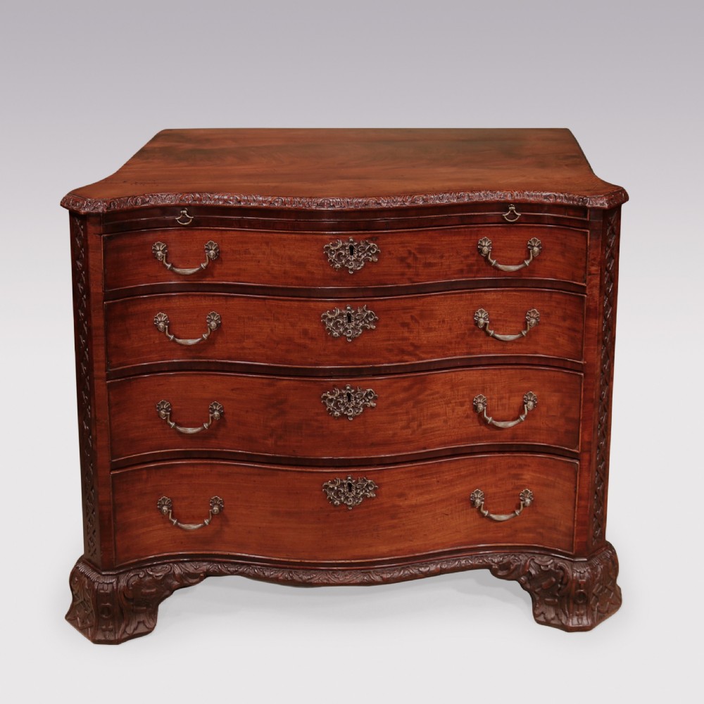 An antique George III mahogany chest of drawers featuring a serpentine front, four graduated drawers with ornamental brass handles, and carved bracket feet.