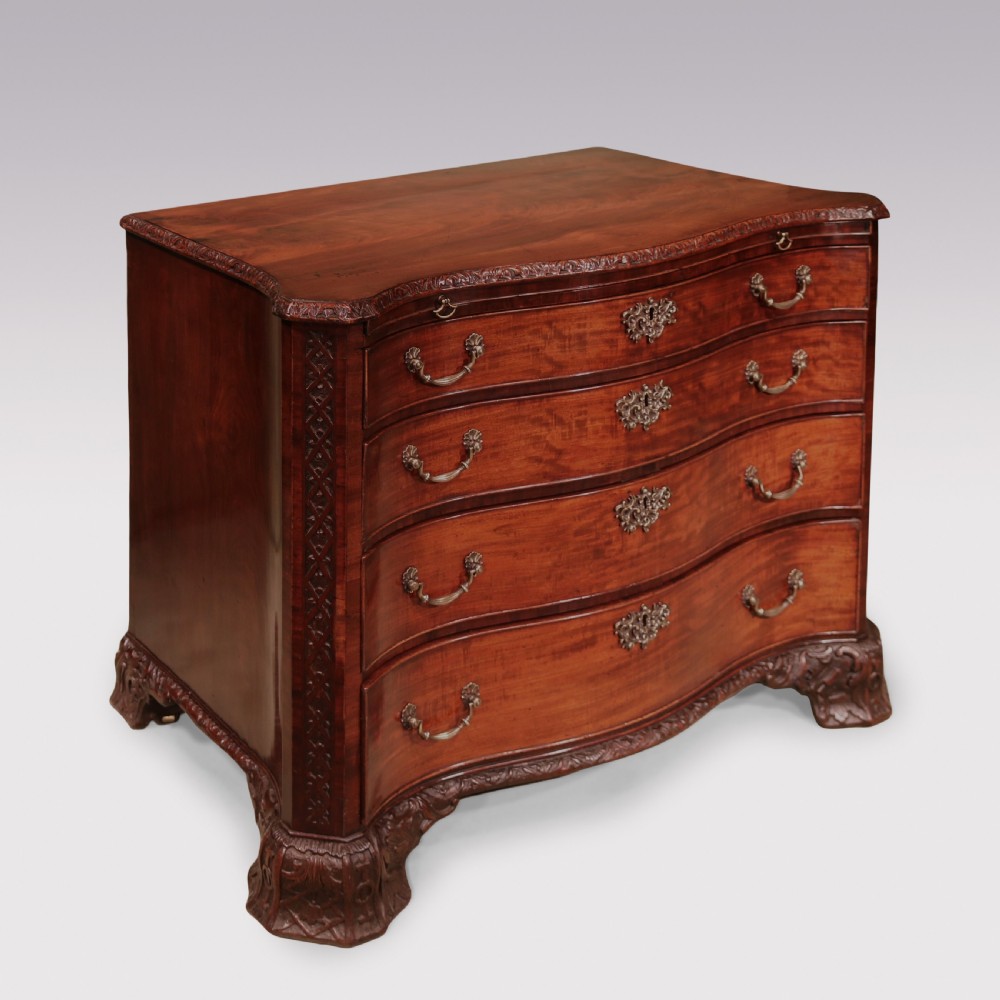 An antique George III mahogany chest of drawers featuring a serpentine front, four graduated drawers with ornamental brass handles, and carved bracket feet. View II