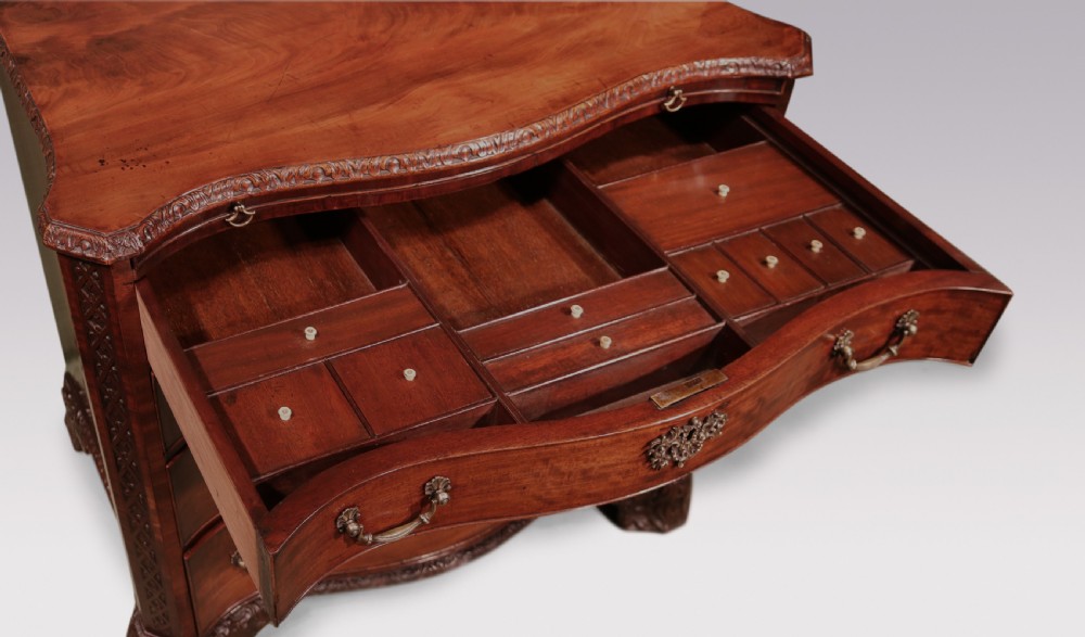 An antique George III mahogany chest of drawers featuring a serpentine front, four graduated drawers with ornamental brass handles, and carved bracket feet. View III