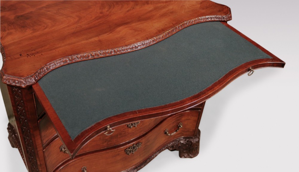 An antique George III mahogany chest of drawers featuring a serpentine front, four graduated drawers with ornamental brass handles, and carved bracket feet. View V