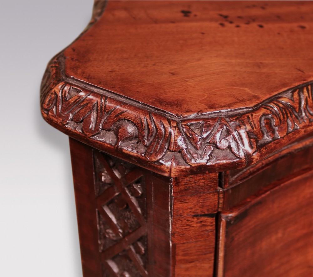 An antique George III mahogany chest of drawers featuring a serpentine front, four graduated drawers with ornamental brass handles, and carved bracket feet. View VII