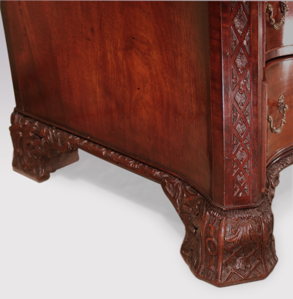 An antique George III mahogany chest of drawers featuring a serpentine front, four graduated drawers with ornamental brass handles, and carved bracket feet. View IX