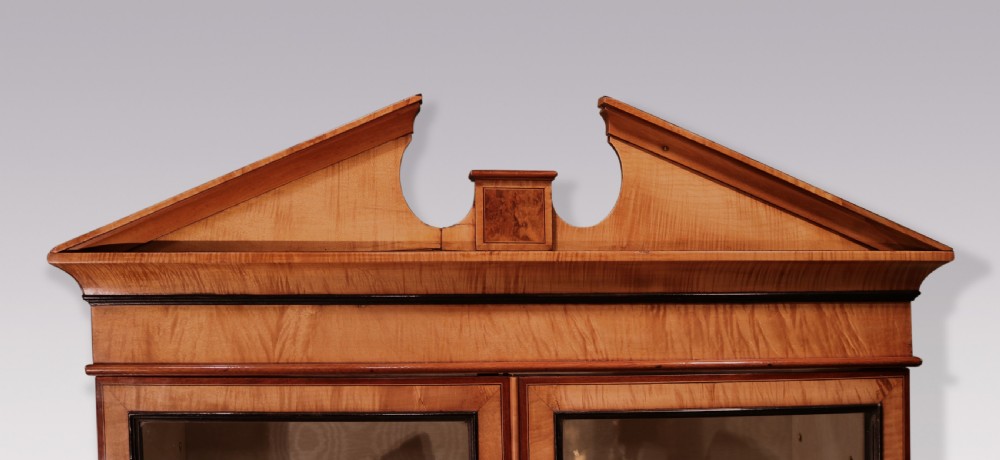 A George III period harewood display cabinet featuring a swan-neck pediment, two glazed doors, two lower drawers, and square tapered legs. View III