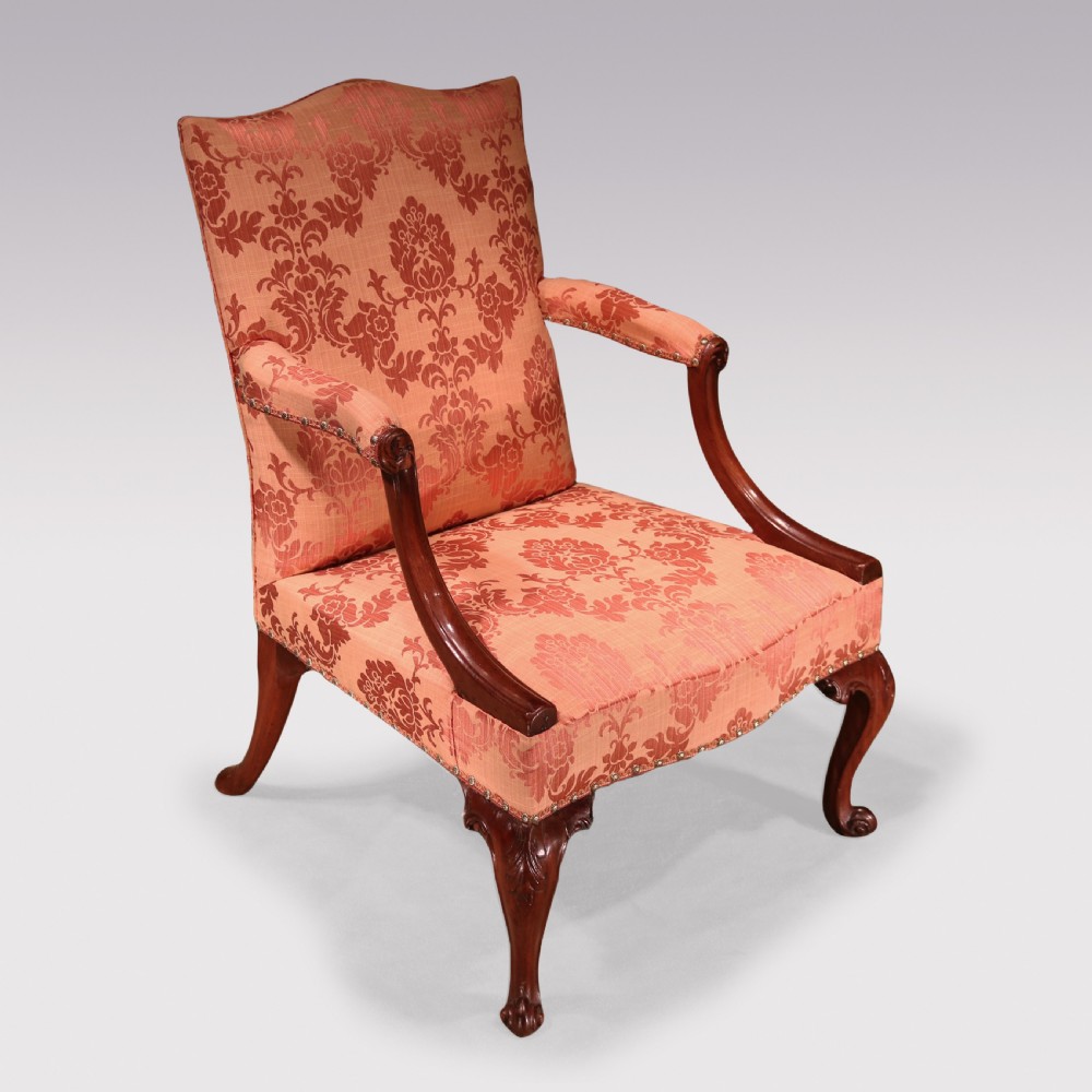 A George III mahogany Gainsborough library armchair upholstered in terracotta floral damask fabric with carved arm supports and cabriole legs.