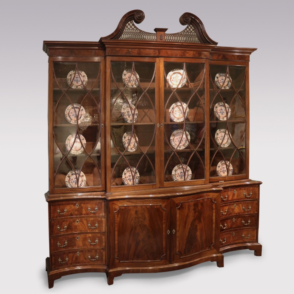 A Georgian Chippendale mahogany breakfront bookcase featuring a swan-neck pediment, lattice fretwork, four glazed doors with oval astragal glazing bars, and a base with drawers and cupboard doors.