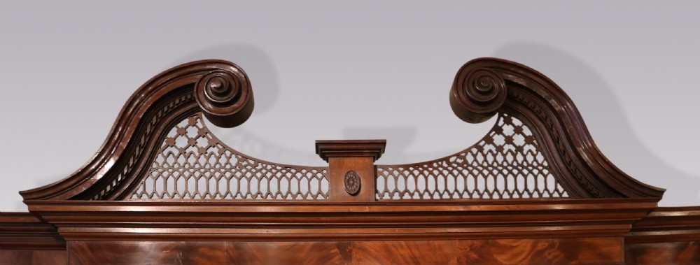 A Georgian Chippendale mahogany breakfront bookcase featuring a swan-neck pediment, lattice fretwork, four glazed doors with oval astragal glazing bars, and a base with drawers and cupboard doors. View III