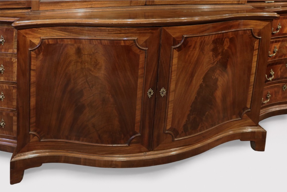 A Georgian Chippendale mahogany breakfront bookcase featuring a swan-neck pediment, lattice fretwork, four glazed doors with oval astragal glazing bars, and a base with drawers and cupboard doors. View V