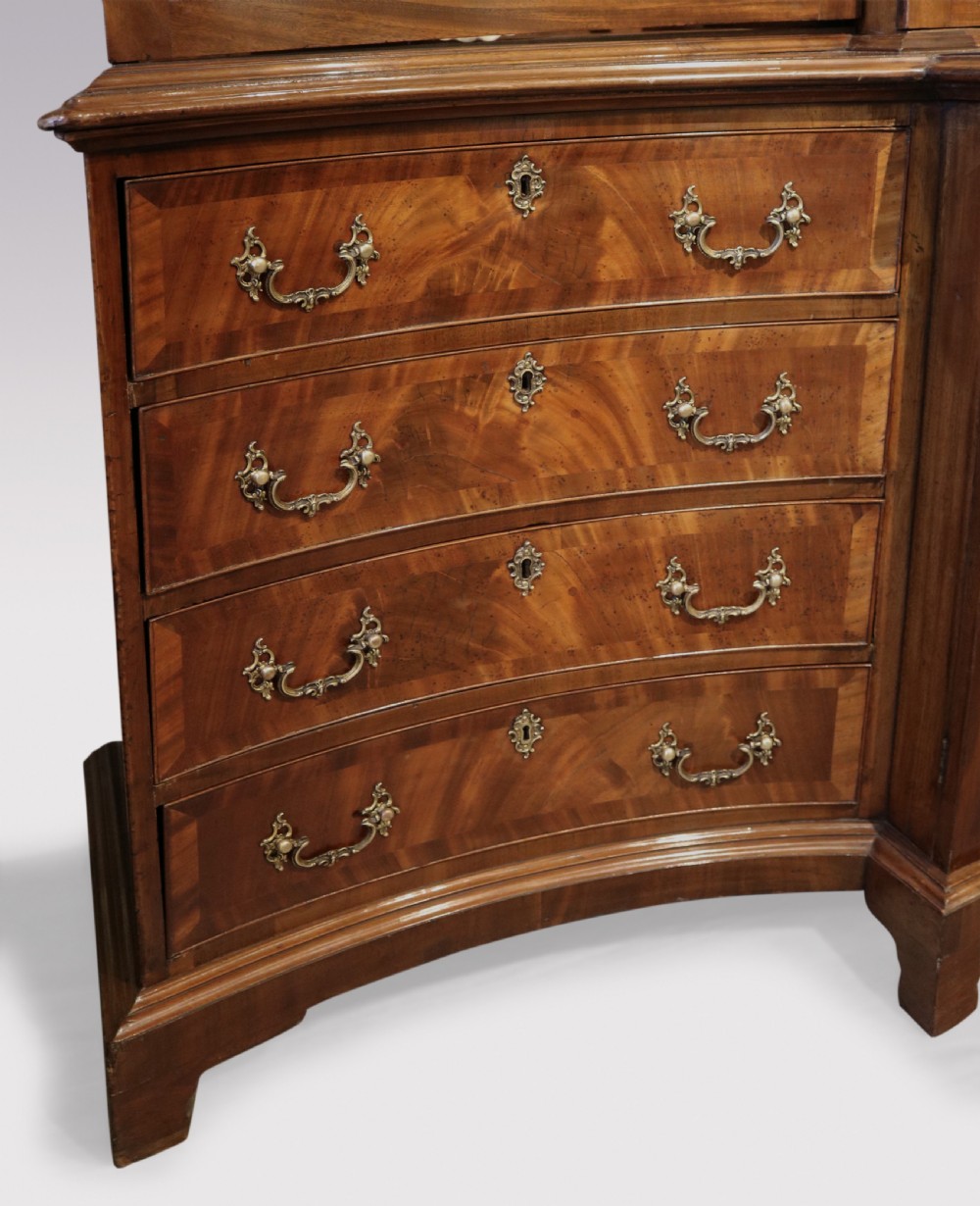 A Georgian Chippendale mahogany breakfront bookcase featuring a swan-neck pediment, lattice fretwork, four glazed doors with oval astragal glazing bars, and a base with drawers and cupboard doors. View VI