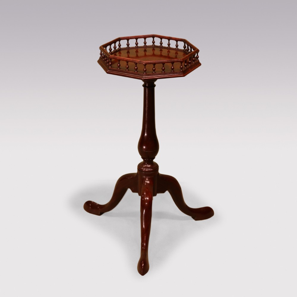 A George II mahogany kettle stand featuring an octagonal spindle-gallereed top supported on a turned central column and tripod cabriole legs.