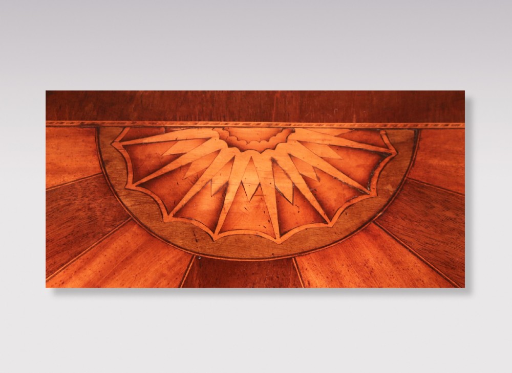 A semi-circular George III satinwood and padoukwood console table featuring a sunburst inlaid top and square tapered legs. View IV