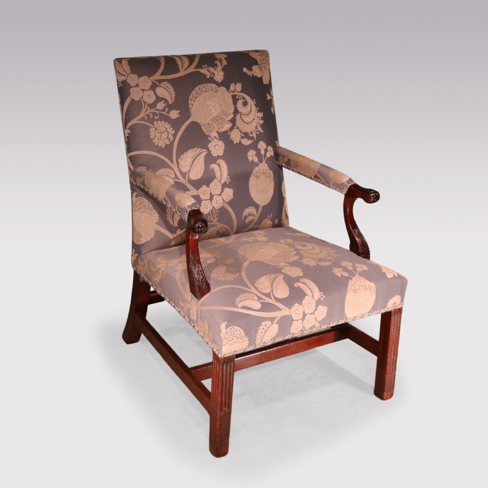 A George III mahogany armchair featuring floral patterned damask upholstery, brass stud detailing, curved carved arms, and fluted square front legs.