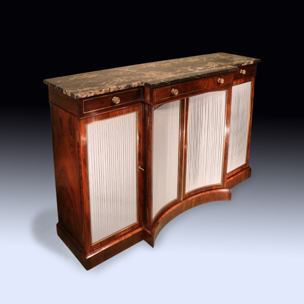 A Regency period rosewood chiffonier featuring a dark marble top, upper drawers with turned knobs, and pleated fabric panelled breakfront doors.