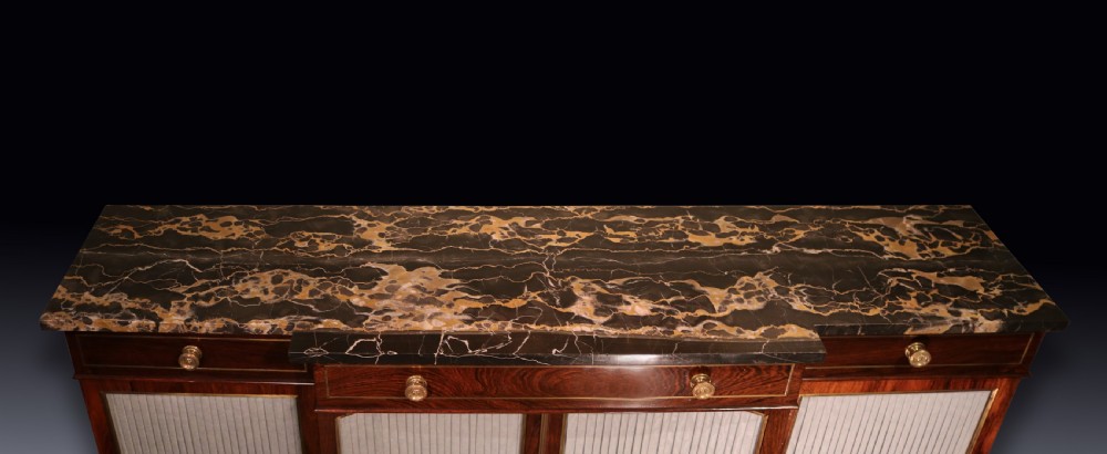 A Regency period rosewood chiffonier featuring a dark marble top, upper drawers with turned knobs, and pleated fabric panelled breakfront doors. View II