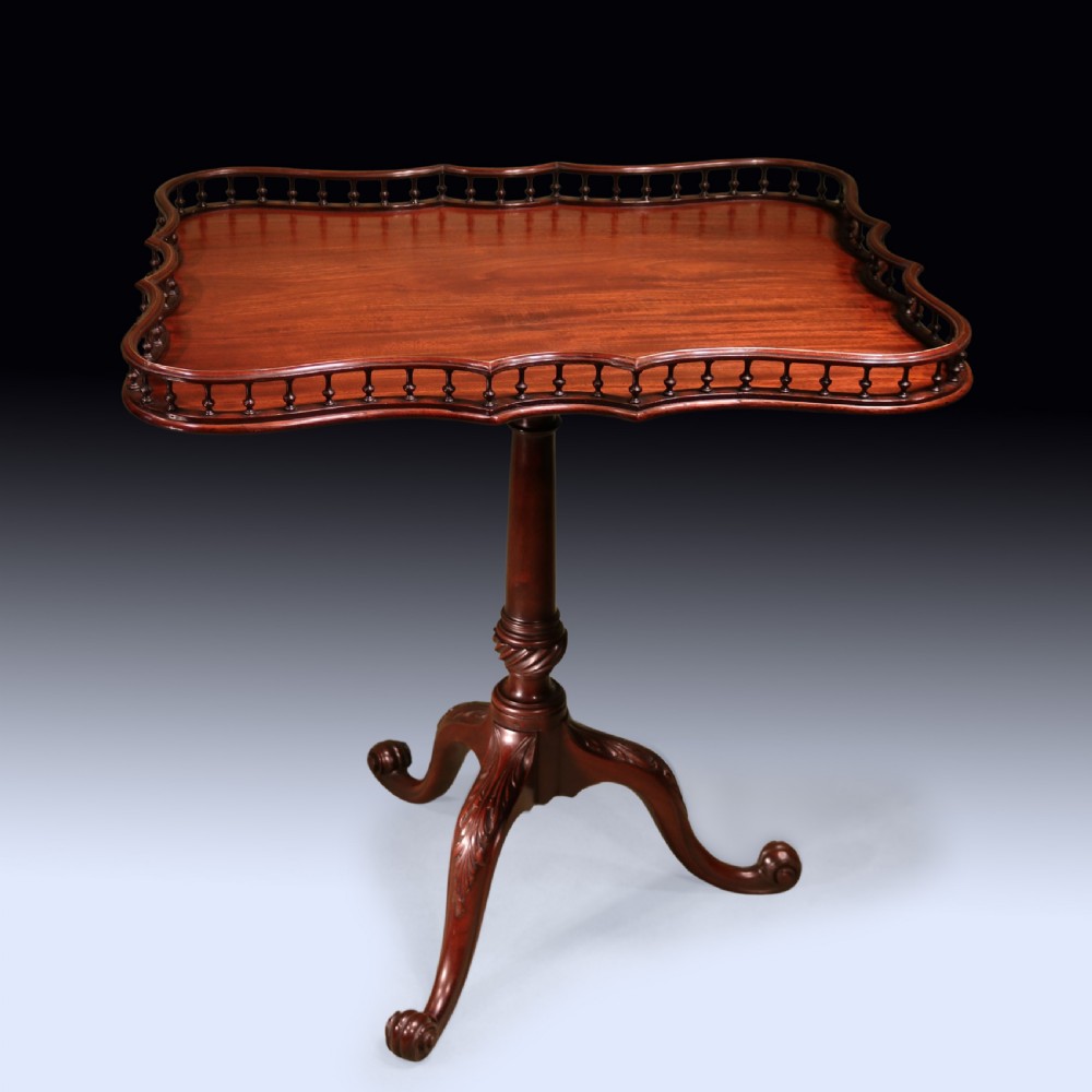 A George III mahogany tripod table featuring a rectangular serpentine top with a pierced spindle gallery on a carved pillar and cabriole legs.